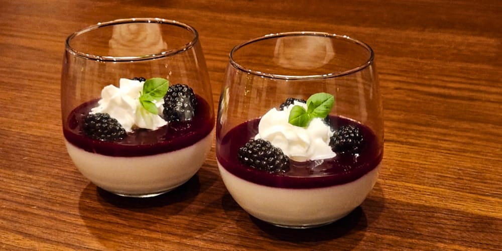 Two servings of panna cotta topped with blackberry sauce, whipped cream, and fresh basil