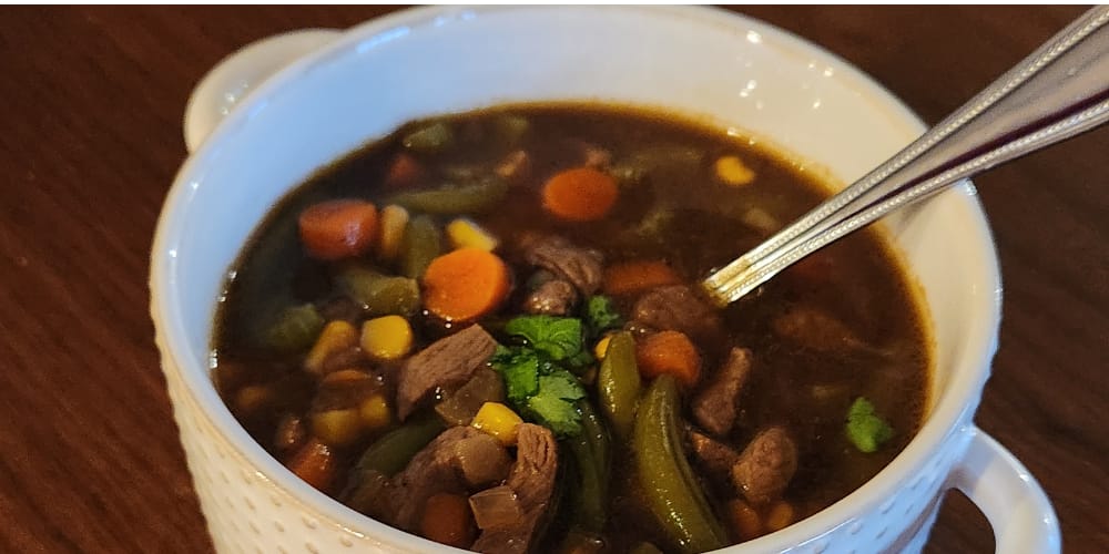 Bowl of vegetable beef soup with corn, carrots, green beans, and garnished with fresh parsley on top