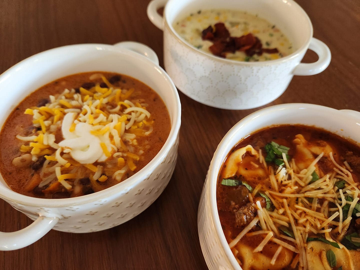 Three bowls with varying soups - a chili, a chicken corn chowder, and a sausage tortellini soup