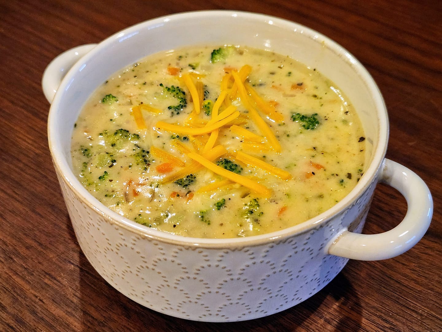 A bowl of broccoli cheddar soup topped with shredded cheddar cheese