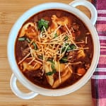 Sausage and tortellini soup in a white soup bowl with handles