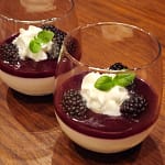 Panna cotta served in stemless wine glasses topped with blackberry sauce, whipped cream, basil sprigs, and fresh blackberries