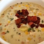 Bowl of creamy chicken corn chowder garnished with bacon crumbles and fresh herbs