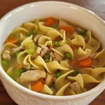Bowl of chicken noodle soup with chicken, carrot, celery, peas