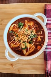 Sausage and tortellini soup in a white soup bowl with handles