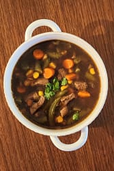 Bowl of soup with beef and vegetables including corn, carrot, green beans and celery