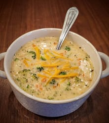 Bowl of creamy soup with broccoli, carrots, and cheddar cheese