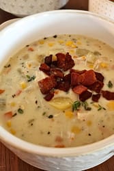 Bowl of creamy chicken corn chowder garnished with bacon crumbles and fresh herbs