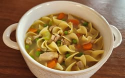 Bowl of chicken noodle soup with chicken, carrot, celery, peas