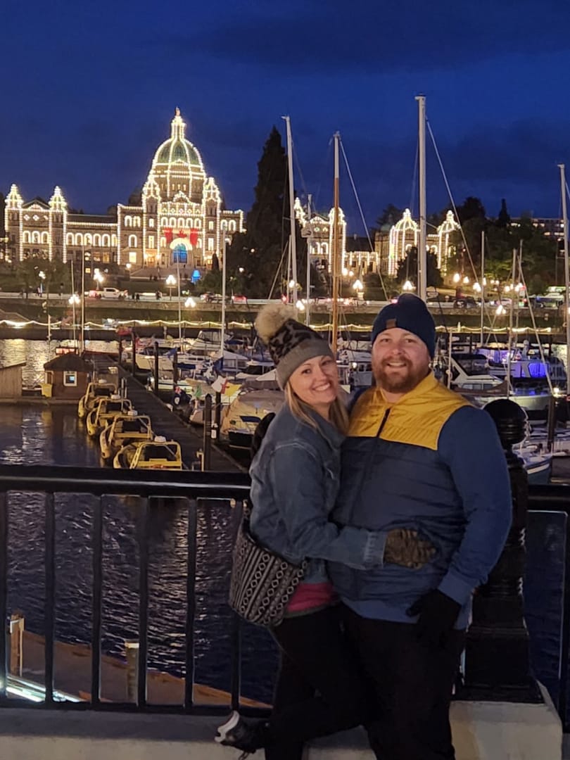 Couple posing in front of the Legislative Building in Victoria, BC, Canada at night with the building lit with lights